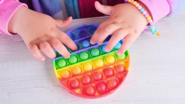 Baby female hands playing with pop it sensory toy circle form. little female presses colorful rainbow squishy soft silicone bubbles on white background. Stress and anxiety relief. Trendy fidgeting — Stock Video