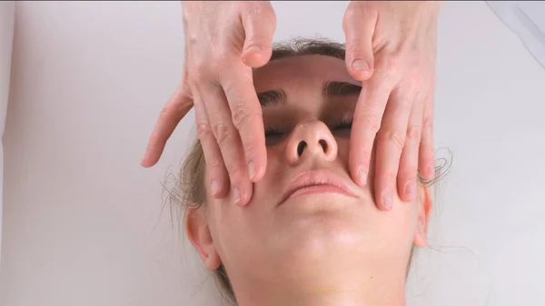 Masaje facial tratamiento de belleza. Primer plano de una cara de mujer joven acostada en la espalda, recibiendo masaje lifting facial, pellizcar y rodar técnica —  Fotos de Stock