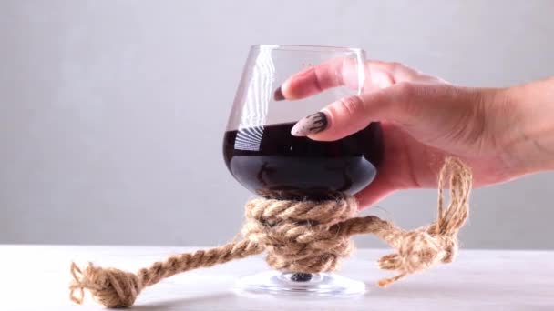 Mão feminina segurando copo de vinho é amarrado com uma corda de juta. O conceito de dependência de álcool. — Vídeo de Stock
