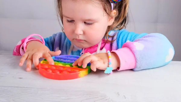 Cute little girls playing with enthusiasm pop it sensory toy circle form. little female presses colorful rainbow squishy soft silicone bubbles on white background. Stress and anxiety relief. Trendy — Stock Photo, Image