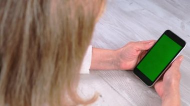 Orta yaşlı bayan sinyora krom ekranlı iPhone akıllı telefonu kullanıyor, fotokopi alanı, üst görünüm. Çevrimiçi alışveriş kavramı, mobil uygulamaların kullanımı: Moskova, Rusya - 24 Haziran 2021.