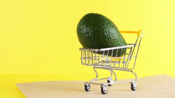 Warenkorb mit Avocado drinnen auf gelbem Hintergrund, Nahaufnahme. Black Friday Shopping und Discount-Konzept. — Stockvideo
