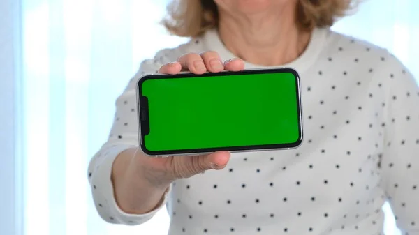 La señora de mediana edad utiliza un teléfono inteligente iPhone con una pantalla de clave de croma, espacio de copia, primer plano. Concepto de compras en línea, uso de aplicaciones móviles: Moscú, Rusia - 24 de junio de 2021. —  Fotos de Stock