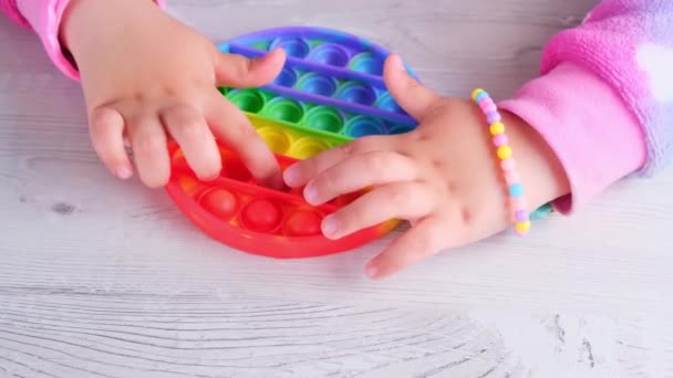 Baby ženské ruce hrát s pop to smyslové hračky kruh tvar. malá samička lisuje barevné duhové měkké silikonové bubliny na bílém pozadí. Stres a úleva od úzkosti. Trendy fidgeting — Stock video