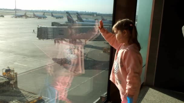 ゲートウィンドウを通ってモスクワ空港の駐車飛行機を見ている少女。連隊のための航空機の維持と準備。休暇、旅行、期待と夢のコンセプト:モスクワ — ストック動画