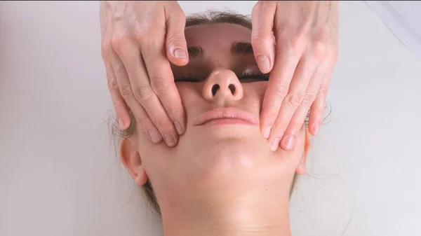 Massaggio viso trattamento di bellezza. Primo piano di una giovane donna faccia sdraiata sulla schiena, ottenere massaggio lifting facciale, pizzicare e rotolare tecnica — Foto Stock