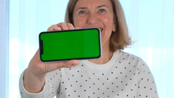 Weibliche Senora mittleren Alters hält und zeigt ein iPhone-Smartphone mit einem Chroma-Schlüssel, Kopierraum. Online-Shopping-Konzept, Nutzung mobiler Anwendungen: Moskau, Russland - 24. Juni 2021. — Stockfoto