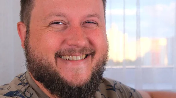 Happy young bearded guy with fashionable hairstyle and beard looking at camera, brightfully smiling with teeth. — Stock Photo, Image