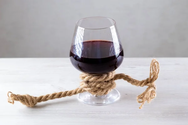 Copo de vinho tinto é amarrado com uma corda. O conceito de dependência de álcool. — Fotografia de Stock