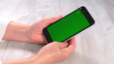 Orta yaşlı kadınlardan yeni normal konseptte ulaşılamıyor ve yeşil ekranlı akıllı telefon kullanılıyor: Moskova, Rusya - 24 Haziran 2021.