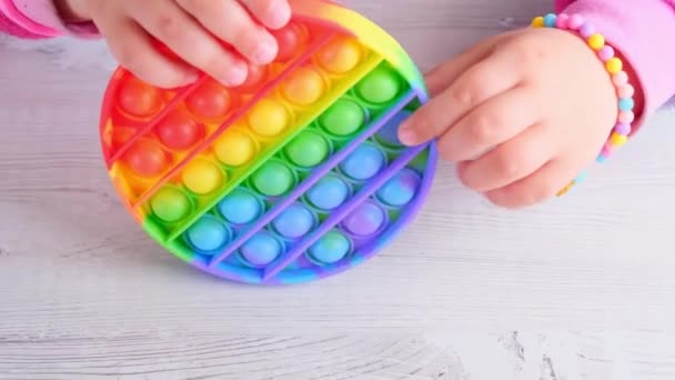 Baby female hands playing with pop it sensory toy circle form. little female presses colorful rainbow squishy soft silicone bubbles on white background. Stress and anxiety relief. Trendy fidgeting — Stock Video