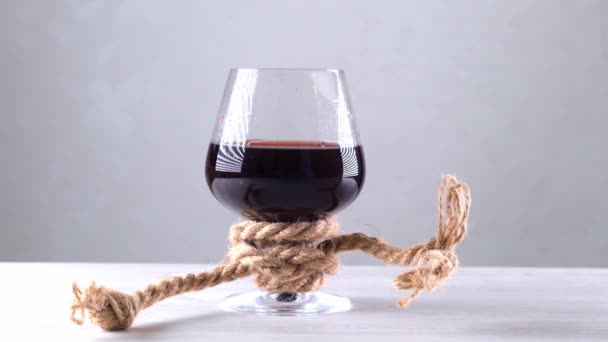 Бокал вина завязан веревкой. Концепция алкогольной зависимости. — стоковое видео
