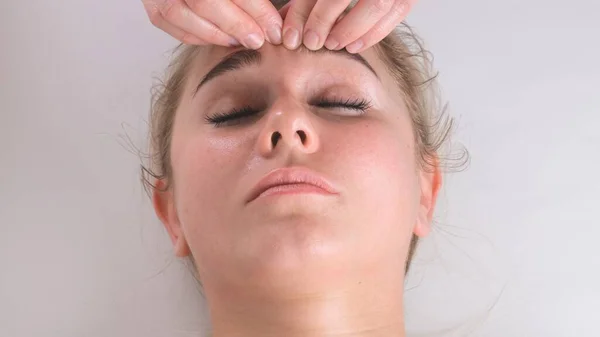 Masaż twarzy zabieg kosmetyczny. Zbliżenie do młodej kobiety twarzy leżącej na plecach, otrzymującej masaż twarzy, technikę szczypania i zwijania — Zdjęcie stockowe