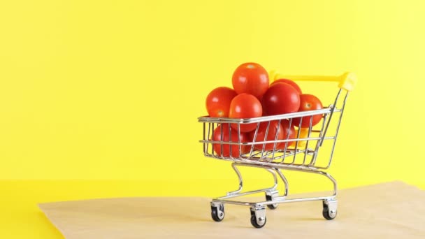 Einkaufswagen mit Kirschtomaten drinnen auf gelbem Hintergrund, Nahaufnahme. Black Friday Shopping und Discount-Konzept — Stockvideo