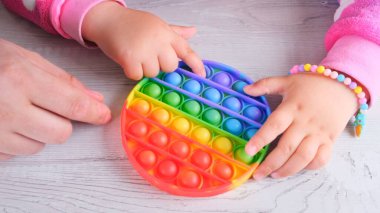 Şirin küçük kızlar babalarıyla oynuyorlar. Duyusal oyuncak çemberi formunda. Küçük dişi, beyaz arka planda renkli gökkuşağı yumuşak silikon kabarcıklar oluşturur. Stres ve endişe giderici. Eğilim