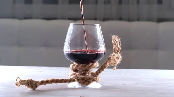 Vinho é derramado em vidro é amarrado com uma corda. O conceito de dependência de álcool. — Fotografia de Stock