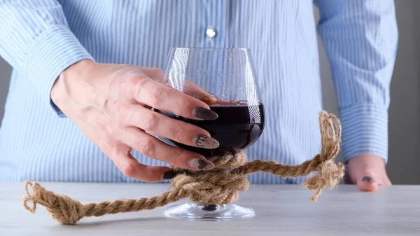 Hona hand hålla vinglas är bunden med en jute rep. Begreppet alkoholberoende. — Stockfoto