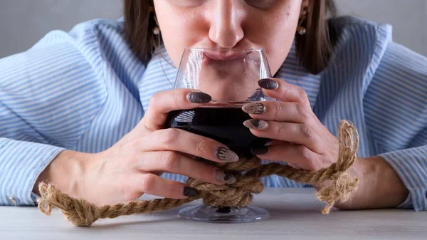 Vrouw grappige drankjes uit een wijnglas gebonden met een jute touw. Het concept van alcoholverslaving. Het probleem van alcoholisme — Stockfoto