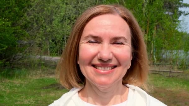 Carismático Hermosa cara de mujer madura. Dama adulta sonriendo al aire libre. Retrato de mujer de 55-60 años relajándose en el jardín. — Vídeos de Stock