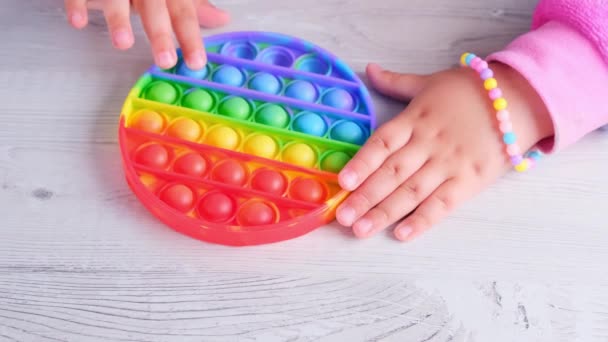 Baby kvinnliga händer leker med pop det sensoriska leksak cirkel form. små kvinnliga pressar färgglada regnbåge squishy mjuka silikonbubblor på vit bakgrund. Stress och ångestlindring. Trendig fidgeting — Stockvideo