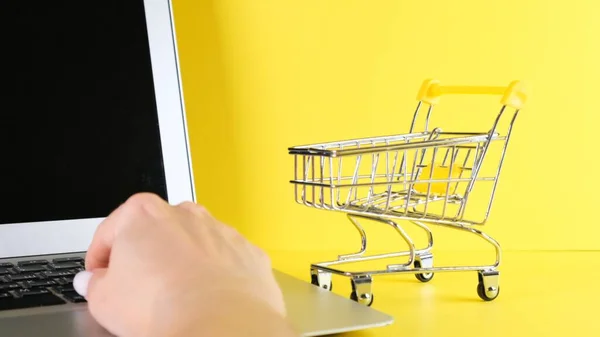 Shopping basket next to a laptop on a yellow background. Copy space. Online shopping concept. — Stock Photo, Image