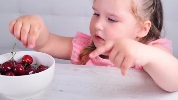 Mooi glimlachend klein schattig meisje zitten met een bord kersen en het eten van een bes — Stockvideo