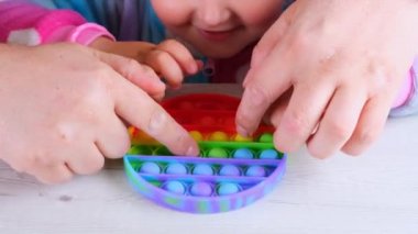 Şirin küçük kızlar babalarıyla oynuyorlar. Duyusal oyuncak çemberi formunda. Küçük dişi, beyaz arka planda renkli gökkuşağı yumuşak silikon kabarcıklar oluşturur. Stres ve endişe giderici. Eğilim