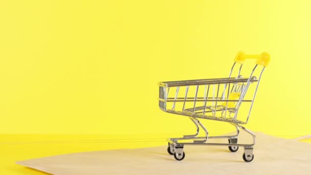 Prázdný nákupní vozík na žlutém pozadí, detailní záběr. Černý pátek Nákupní a slevy koncept — Stock video