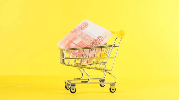 Nákupní vozík s bankovkou pěti tisíc rublů na žlutém pozadí, detailní záběr. Černý pátek Nákupní a slevy koncept — Stock fotografie