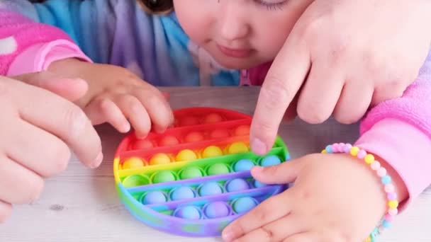 Şirin küçük kızlar babalarıyla oynuyorlar. Duyusal oyuncak çemberi formunda. Küçük dişi, beyaz arka planda renkli gökkuşağı yumuşak silikon kabarcıklar oluşturur. Stres ve endişe giderici. Eğilim — Stok video