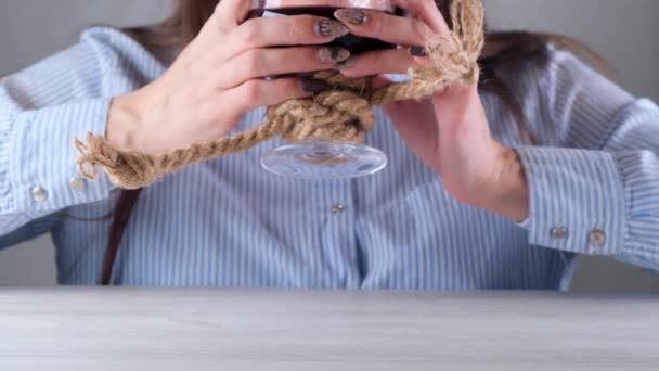 Manos femeninas levantan copa de vino está atado con una cuerda de yute. El concepto de dependencia al alcohol. El problema del tratamiento del alcoholismo — Vídeo de stock