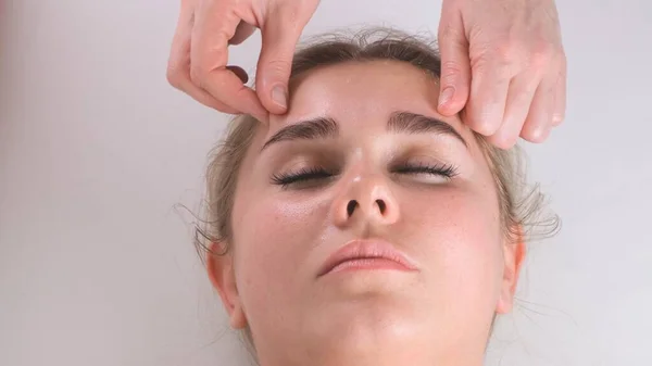 Masaje facial tratamiento de belleza. Primer plano de una cara de mujer joven acostada en la espalda, recibiendo masaje lifting facial, pellizcar y rodar técnica —  Fotos de Stock