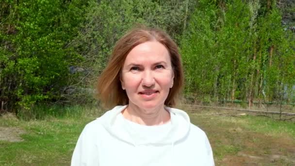 Hermosa cara de mujer madura. Dama adulta sonriendo al aire libre. Retrato de mujer de 55-60 años relajándose en el jardín. — Vídeo de stock