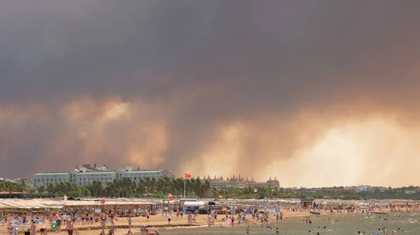 Füst az erdőtüzek emelkedik a strand felett Antalya, Manavgat üdülőhely város Törökország. View with people on the beach: Antalya, Manavgat Törökország - július 28, 2021. — Stock Fotó