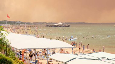 Türkiye 'nin Manavgat tatil beldesi Antalya' da bir plajda orman yangınlarından çıkan duman. Sahilde insanlarla görüntüleme: Antalya, Manavgat Turkey - 28 Temmuz 2021.