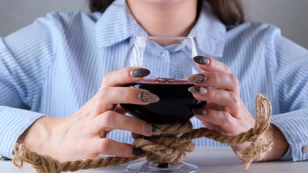 Manos femeninas sosteniendo copa de vino está atado con una cuerda de yute. El concepto de dependencia al alcohol. El problema del tratamiento del alcoholismo — Foto de Stock