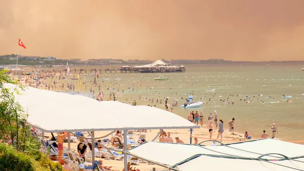 Fumo da incendi boschivi che salgono sopra una spiaggia in Antalya, la città di resort di Manavgat della Turchia. Vista con la gente sulla spiaggia: Antalya, Manavgat Turchia - 28 luglio 2021. — Foto Stock