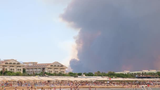 Rook van bosbranden die opkomen boven een strand in Antalya, de badplaats Manavgat in Turkije. Uitzicht met mensen op het strand: Antalya, Manavgat Turkije - 28 juli 2021. — Stockvideo