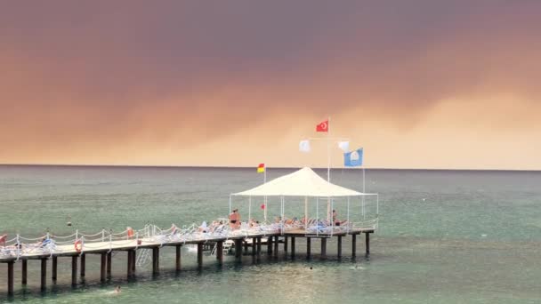 Kouř z lesních požárů stoupající nad pláží v Antalyi, letovisko Manavgat v Turecku. Pohled s lidmi na pláži: Antalya, Manavgat Turecko - 28. července 2021. — Stock video