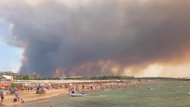 Fumaça de incêndios florestais subindo sobre uma praia em Antalya, cidade turística de Manavgat. Vista com as pessoas na praia: Antalya, Manavgat Turquia - 28 de julho de 2021. — Vídeo de Stock