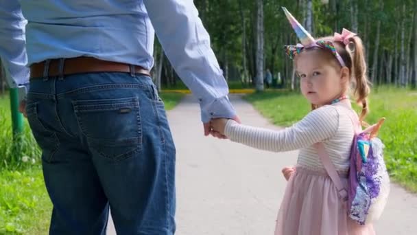 Веселые папа и дочь 3-4 лет идут и держатся за руки на прогулке в парке. День отца. Счастливое детство. вид сзади — стоковое видео