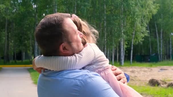 Счастливый отец носит вокруг шеи и обнимает дочь 4-5 лет во время прогулки по парку — стоковое видео