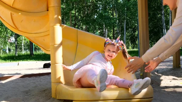 Vrolijke moeder die haar dochter beneden van de glijbaan ziet glijden. Grappige familieactiviteit in het park, plezier hebben. Happy childhood concept: Moskou, Rusland - 18 augustus 2021 — Stockfoto