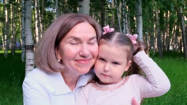 Портрет обнімаючої пари бабусі її маленька 3-річна онучка сміється і притискає один до одного ніжні щоки, одягнені в світло-білий рожевий одяг. Концепція міжгенерації — стокове відео