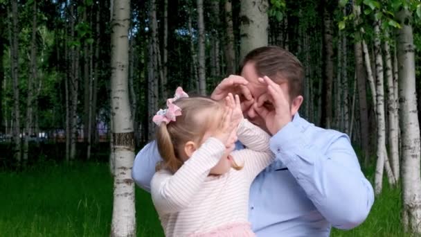 Mała córeczka 3 lata i ojciec bawią się na ulicy, robiąc śmieszne miny, robiąc okulary palcami, jak okulary patrzące w kamerę przez lornetkę. baw się dobrze z dzieckiem — Wideo stockowe