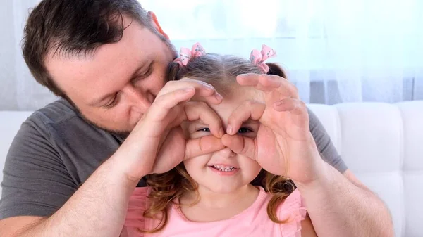 Filhinha de 3 anos e pai estão se divertindo em casa, fazendo caras engraçadas, fazendo óculos com os dedos, como óculos olhando para a câmera através de binóculos. divirta-se com a criança, livre — Fotografia de Stock