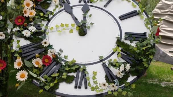 Великий настінний годинник на полі в квітучих квітах, показує час 11:55, 12:00. концепція управління часом, час переходу на літній час. Весна чи весілля. Пікнік для жіночого дня — стокове відео