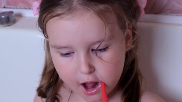 Little pretty girl 3 years old brushes her teeth with a red toothbrush in the bathroom at home. Health care, dental hygiene, people and beauty concept — Stock Video