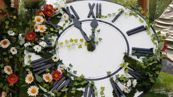 Relógio de parede grande no campo em flores florescendo, mostrando o tempo 11: 55, 12: 00. conceito de gerenciamento de tempo, horário de verão. Primavera ou casamento. Piquenique de dia de mulheres — Fotografia de Stock