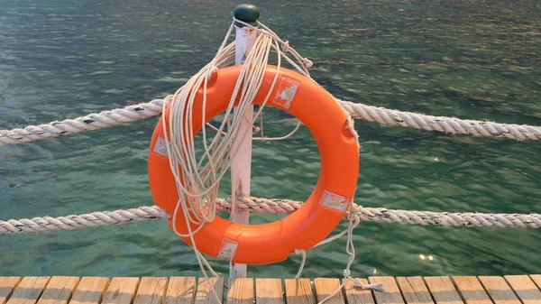 Orange lifeline and sea ropes on the background of the sea and blue sky. Marine ropes and life preserver hanging on a post. Help and safety concept — Stock Photo, Image